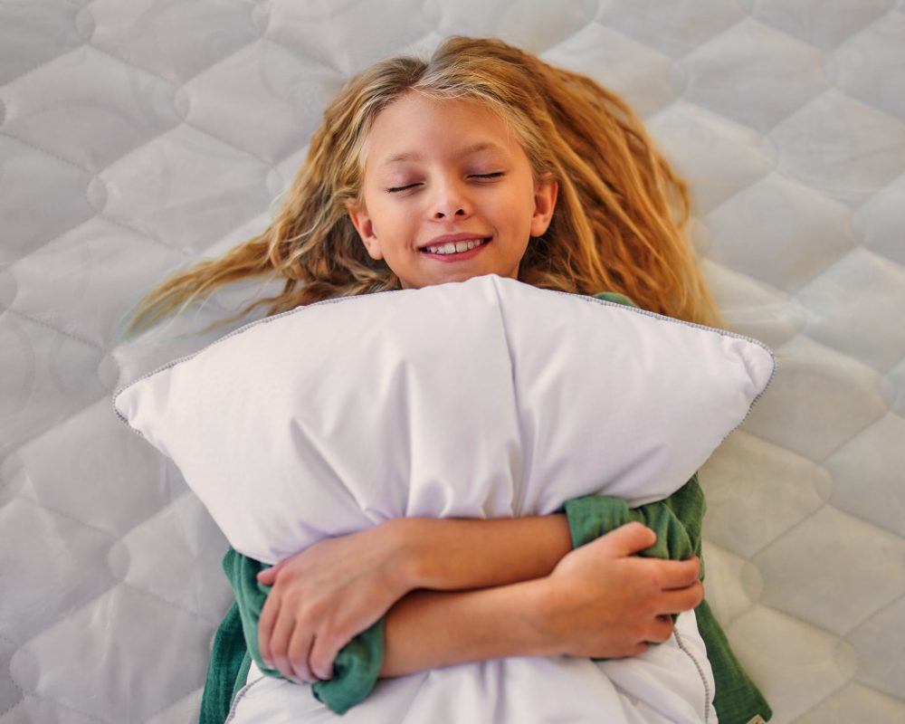 Beautiful child cute girl lying on the bed and hugging a pillow in the store. Purchase of bedding, mattress and bed.